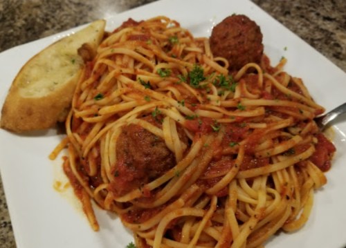 A plate of spaghetti with meatballs, marinara sauce, and a slice of garlic bread, garnished with parsley.