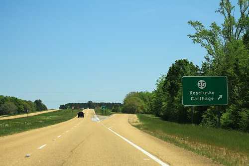 A highway sign indicating a right turn for Kosciusko and Carthage, with a clear blue sky and green trees in the background.