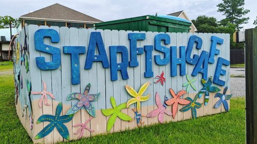Colorful wooden sign reading "STARFISH CAFE" on a fence, decorated with painted starfish and flowers.