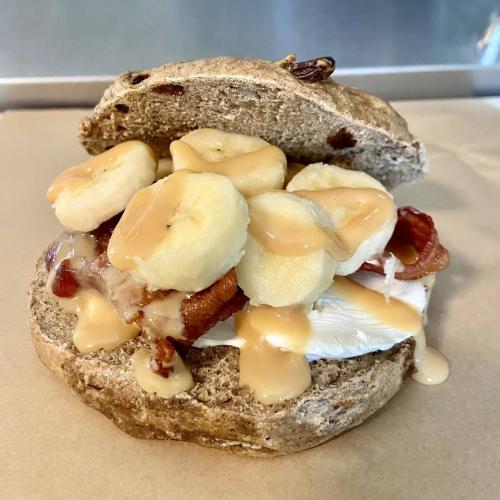 A sandwich with whole grain bread, cream cheese, bacon, banana slices, and drizzled with peanut butter.