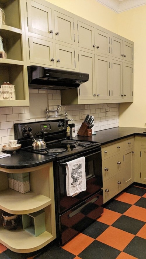 A modern kitchen with green cabinets, black appliances, and a checkered orange and black floor.