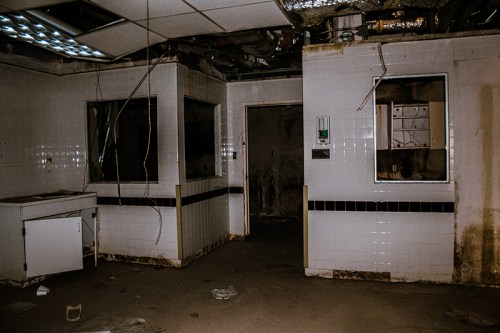 Abandoned room with dirty white tiles, broken windows, and exposed wires, creating a desolate atmosphere.