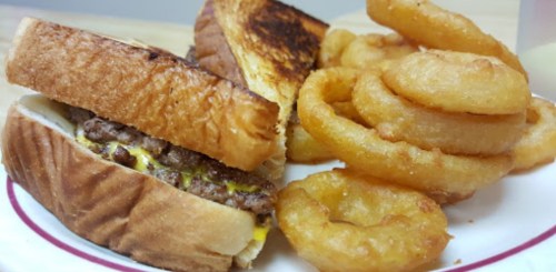 A plate with a grilled sandwich filled with beef and mustard, alongside crispy onion rings.