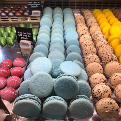A display of colorful macarons and chocolates, featuring blue, yellow, and pink treats in neat rows.