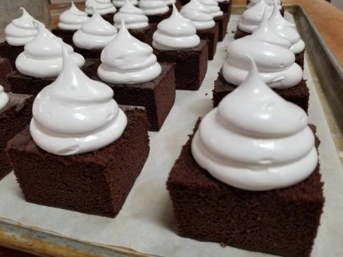 A tray of chocolate cake squares topped with fluffy white meringue swirls.