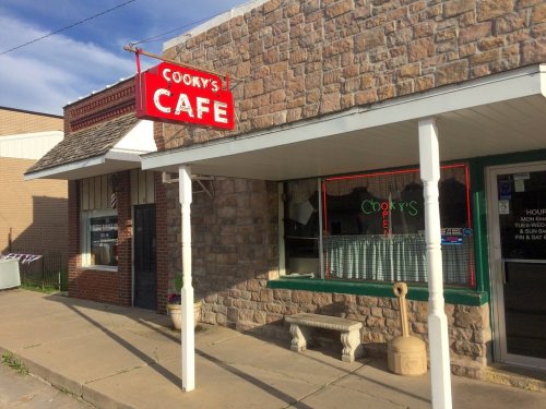 Exterior of Cooky's Café, featuring a stone facade, red sign, and a bench outside on a sunny day.