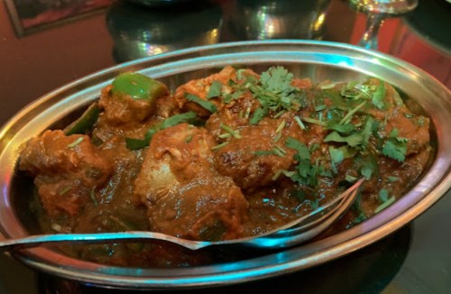 A silver serving dish filled with spicy chicken curry, garnished with fresh cilantro and green peppers.