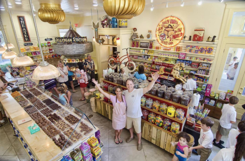A vibrant candy shop filled with colorful treats, featuring a couple joyfully posing in front of a display of sweets.
