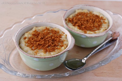 Two bowls of creamy dessert topped with crushed cookies, placed on a decorative plate with a spoon beside them.