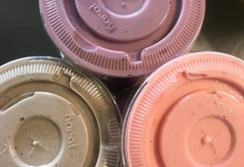 Three smoothie cups with colorful lids: pink, purple, and green, stacked together.