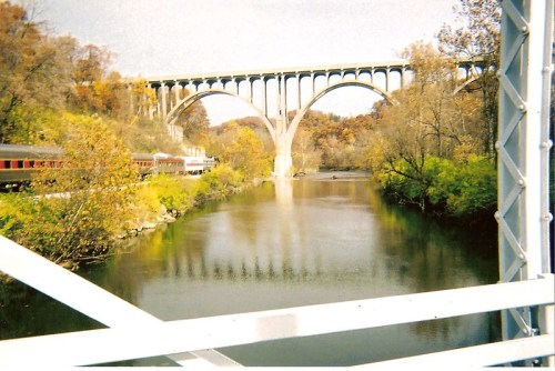 A scenic view of a bridge over a river, surrounded by autumn foliage and a train passing nearby.