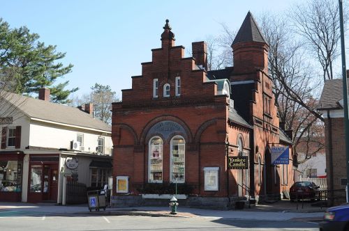 Historic brick building with a unique architectural design, featuring a tower and large windows, in a quaint town setting.