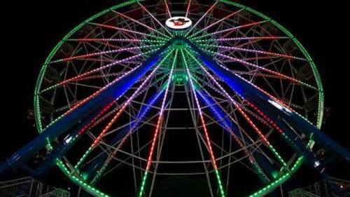 A brightly lit Ferris wheel at night, featuring colorful green, red, and blue lights against a dark sky.