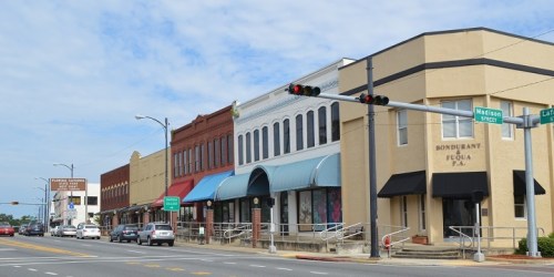 A street view of a small town with historic buildings, shops, and traffic lights under a cloudy sky.