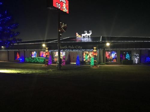 A festive building decorated with colorful Christmas lights, featuring trees and holiday figures, under a night sky.