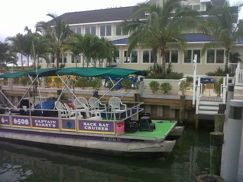 A colorful boat docked by a waterfront restaurant surrounded by palm trees and greenery.