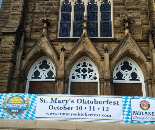 Banner for St. Mary's Oktoberfest, featuring dates October 10-12, displayed on a stone church facade.