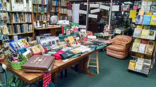 A cozy bookstore display with a wooden table filled with books, holiday decorations, and two comfortable chairs nearby.