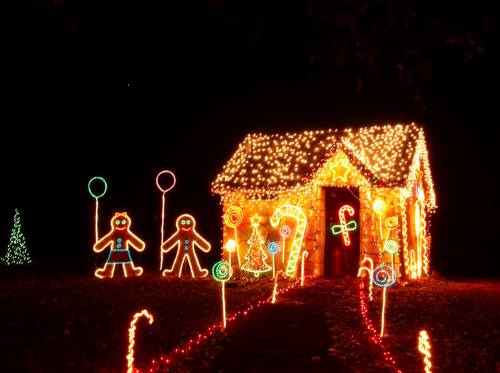 A brightly lit gingerbread house decorated with colorful Christmas lights and festive figures in a dark night setting.