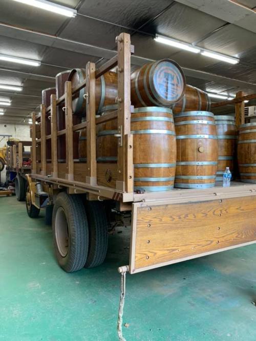 A wooden truck loaded with large barrels, parked indoors on a green floor.