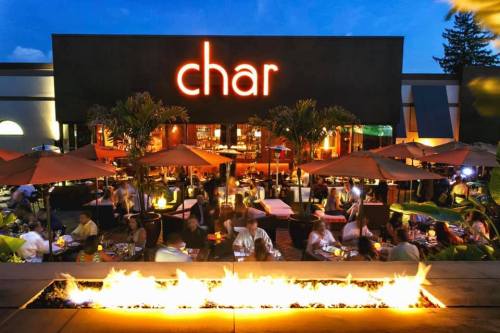Outdoor dining scene at night with a vibrant restaurant sign, surrounded by patrons and illuminated by fire features.