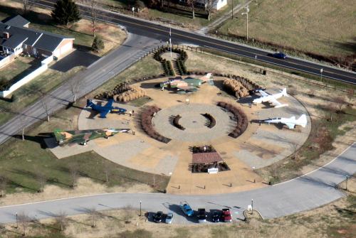 Aerial view of a circular park featuring various military aircraft displayed around a central garden area.