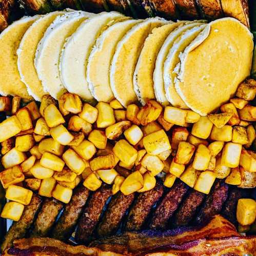 A colorful breakfast spread featuring pancakes, golden potatoes, sausage links, and crispy bacon.