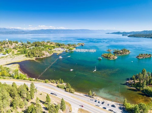 Aerial view of a serene lake with boats, islands, and a winding road lined with trees under a clear blue sky.