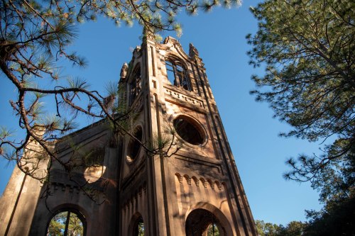 A tall, weathered stone tower surrounded by trees against a clear blue sky.