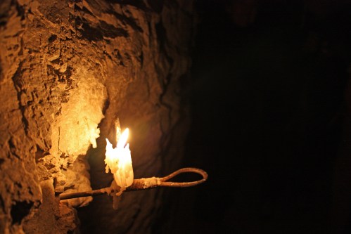 A lit candle mounted on a rocky wall, casting a warm glow in a dark, cavernous space.