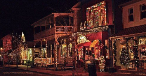 A festive street scene at night, adorned with colorful Christmas lights and decorations on shops and trees.