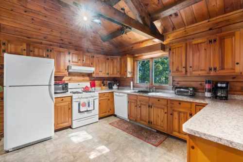 Cozy wooden kitchen with a white fridge, stove, and ample cabinetry, featuring a window with a view.