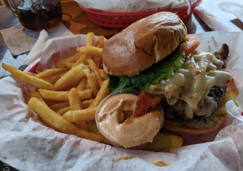 A juicy burger with lettuce, tomato, and cheese, served with crispy fries and a dipping sauce in a red basket.
