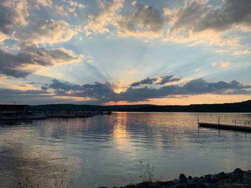 Sunset over a calm lake, with colorful clouds and rays of light reflecting on the water's surface.