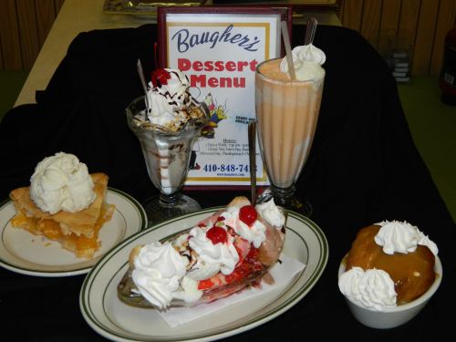 A display of desserts including ice cream sundaes, a milkshake, pie, and a banana split, with a dessert menu in the background.
