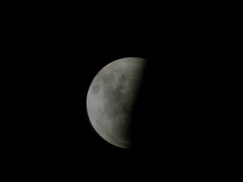 A close-up view of the moon partially shadowed, showcasing its craters and surface details against a dark background.