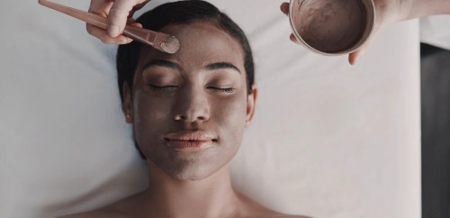 A person receiving a facial treatment, with a clay mask being applied to their face.