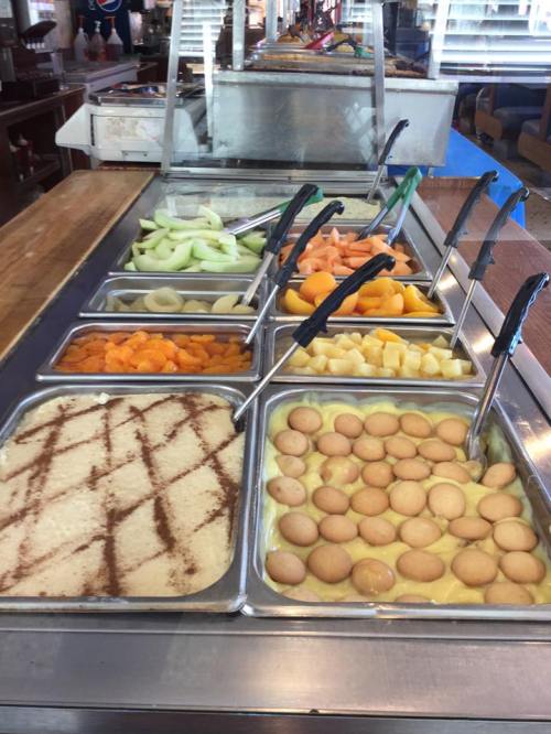 A buffet display featuring various fruits and a dessert with cookies, arranged in metal trays.