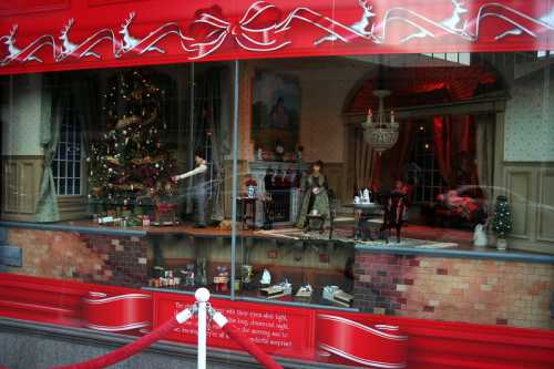 A festive holiday window display featuring a decorated Christmas tree and animated figures in a cozy room setting.