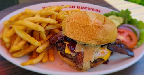 A juicy burger with cheese and sauce, served with crispy fries, lettuce, tomato, and pickles on the side.