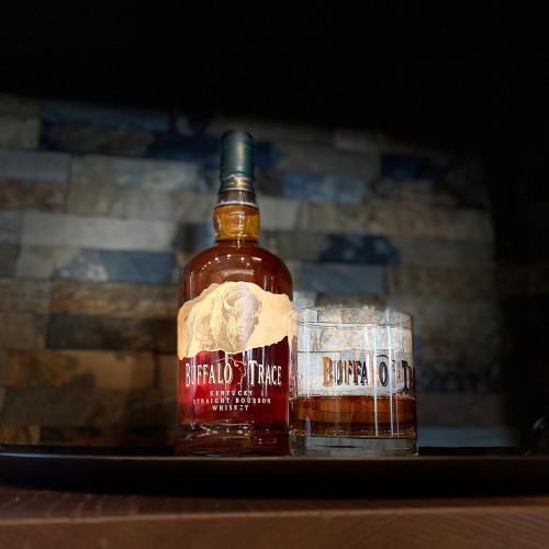 A bottle of Buffalo Trace bourbon next to a glass filled with whiskey, set against a rustic background.