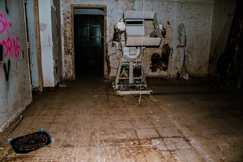 An abandoned room with peeling walls, a rusty machine in the center, and a circular object on the floor.