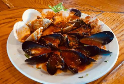 A plate of mussels and clams in a rich tomato sauce, garnished with herbs, on a wooden table.