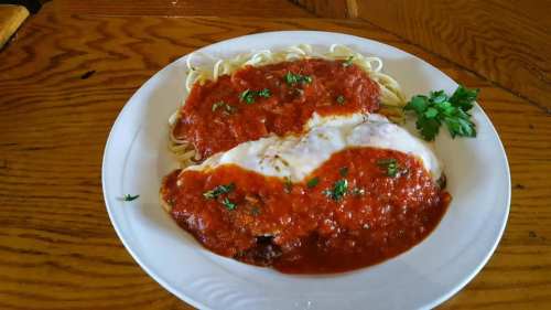 A plate of spaghetti topped with marinara sauce and a breaded chicken cutlet, garnished with parsley.
