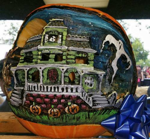 A carved pumpkin featuring a haunted house design, with a blue bow and spooky elements like ghosts and pumpkins.
