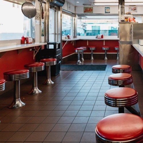 A retro diner interior with red stools, chrome accents, and a clean, empty seating area.