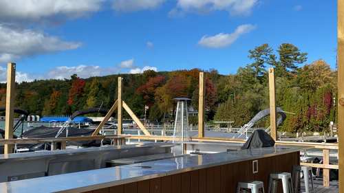 A scenic view of a marina with autumn foliage, blue skies, and boats docked in the background.