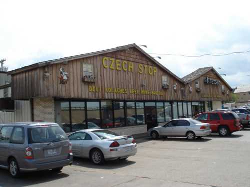 A wooden building with "Czech Stop" signage, featuring cars parked outside and a cloudy sky above.