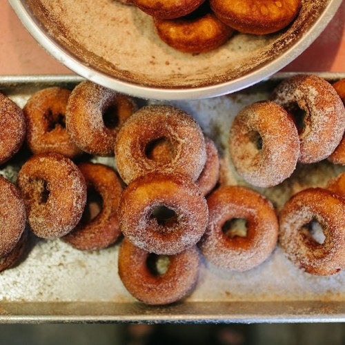 A tray of freshly made, cinnamon-sugar coated donuts arranged neatly, with a bowl of more donuts in the background.