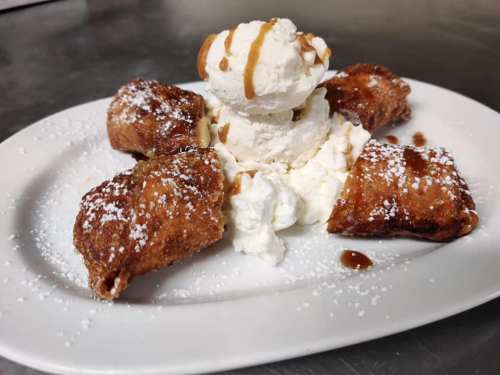 A plate with fried pastries, whipped cream, and ice cream drizzled with caramel sauce, dusted with powdered sugar.
